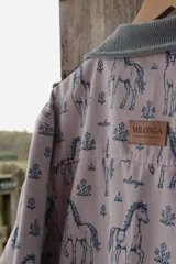 Campera de lona estampada con diseño de caballos y flores, con cuello de pana en color gris azulado y cierre frontal metálico. El interior está forrado en tela de viyela a cuadros.