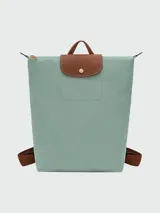 Mochila de diseño minimalista en color beige, con solapa y asa superior en cuero marrón texturizado. Cuenta con correas ajustables en color marrón y cierre principal.