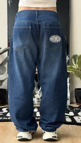 Pantalón de jean azul oscuro de corte wide leg, con diseño holgado y tiro medio. Presenta un pequeño bordado con alas en el bolsillo delantero.