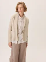 Saco de lana hervida en color beige, con cuello solapa, cierre frontal de botones rústicos y bolsillos frontales. Presenta un diseño clásico con textura delicada y detalles de coderas.