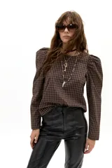 Blusa de popelina de algodón con estampado de cuadros en tonos marrón y blanco. Presenta cuello a la base, mangas largas con hombros abullonados y cierre posterior con botones.