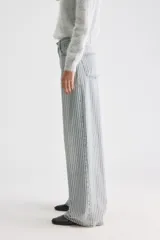Pantalón jean de tiro medio y corte holgado con pernera ancha, diseño a rayas verticales celestes y blancas, confeccionado en algodón rígido.