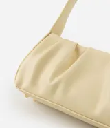Cartera tipo baguette marca Satinato, confeccionada en PU color beige, con diseño estructurado, detalles fruncidos laterales y asa fija para el hombro.