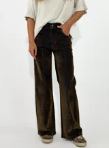 Pantalon de corte recto y tiro medio, confeccionado en denim con acabado aterciopelado en tono marrón oscuro. Presenta costuras verticales marcadas en contraste y cierre frontal con botón y cremallera.