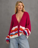 Cardigan tejido de punto en color fucsia, con escote en V y cierre frontal de botones. Presenta un diseño de ondas multicolor en la parte inferior y en los puños, con mangas largas de corte holgado.