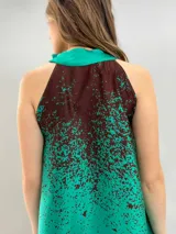 Blusa de satén con escote halter y cuello elevado anudado lateralmente. Presenta un diseño estampado degradado en tonos verde esmeralda y azul, con corte holgado y caída fluida.
