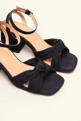 Sandalia de tacón cuadrado medio, confeccionada en terciopelo negro. Presenta un diseño de tiras cruzadas con nudo en la parte delantera y una tira ajustable con hebilla en el tobillo.