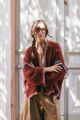 Saco oversize de tejido de punto en color beige, con mangas caídas y detalles de bordado a mano en tonos verde y lila en los bordes y costuras.