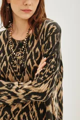 Sweater de punto con cuello redondo y manga larga, presentando un estampado tipo ikat o animal print abstracto en tonos marrón claro y negro/gris oscuro.