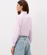 Camisa cropped de manga larga en tejido tricoline, con estampado de rayas verticales finas en color rosa y blanco. Presenta cuello camisero tradicional y cierre frontal decorado con tres lazos de tela. Diseño de corte corto y ajuste recto.