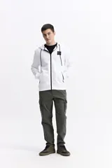 Campera con capucha de algodón y poliéster, color blanco, con cierre frontal negro y cordones negros en la capucha. Presenta un pequeño parche cuadrado negro con texto blanco en el pecho izquierdo y cierres negros en los bolsillos laterales.