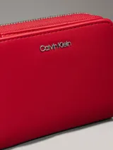 Billetera de piel sintética roja con cierre perimetral de cremallera y logo metálico de Calvin Klein en el frente. Posee 8 ranuras para tarjetas, billetero y bolsillo monedero con cremallera.