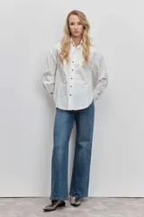 Camisa de corte clásico y calce holgado, color blanco, con cuello camisero, cierre frontal de botones y mangas largas con puños abotonados.
