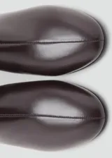 Botín de cuero vacuno color marrón oscuro con tacón bloque de 5,5 cm y cierre de cremallera en la parte posterior. Presenta punta redonda y diseño minimalista.