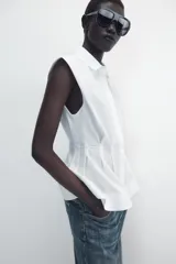 Camisa de cuello solapa y manga sisa, de color blanco. Presenta bajo acabado en peplum y cierre frontal con botones ocultos.