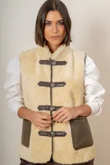 Chaleco de piel ovina con interior de corderito, diseño sin mangas y cierre frontal con trabas de cuero y botones metálicos. Incluye bolsillos laterales de cuero.