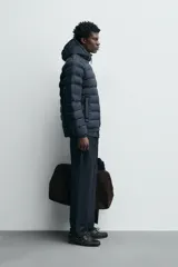Campera puffer acolchada de corte regular fit en color negro, confeccionada en tejido técnico repelente al agua. Presenta cuello subido con capucha, cierre frontal de cremallera, mangas largas con puños elásticos y bolsillos laterales de vivo.