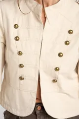 Chaqueta corta color beige de algodón, de inspiración militar con cuello mao y doble botonadura frontal con botones metálicos dorados.