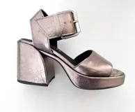 Sandalias de tacón con plataforma color plateado, con tira ancha sobre los dedos y tira con hebilla al tobillo.