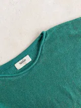 Buzo de tejido de punto con acabado brillante, confeccionado con hilado italiano. Presenta cuello redondo, mangas largas acampanadas y un corte holgado.