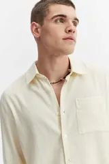 Camisa rústica de manga larga color gris oscuro, con cuello clásico, cierre frontal con botones y un bolsillo aplicado en el pecho.