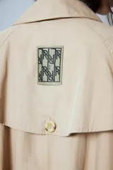 Trench midi color camel confeccionado en algodón y nylon repelente al agua, con cuello clásico, cierre frontal con un botón, bolsillos laterales y tajos laterales. Tiene etiqueta RENÉE en la espalda.