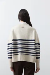 Polera de tejido de punto con diseño a rayas horizontales en color azul marino sobre base beige. Presenta cuello alto, mangas largas con puños acanalados y una silueta relajada.