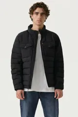 Campera puffer negra con diseño acolchado horizontal, cuello alto, cierre frontal y bolsillos superiores con solapa y botón a presión. Presenta etiqueta roja distintiva de la marca en el pecho.