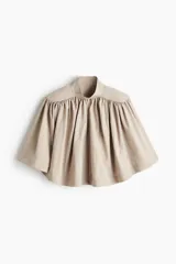 Blusa capa color beige con cuello alto, hombreras y diseño acampanado con frunces.