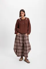 Pantalón de corte holgado con silueta tipo balloon, confeccionado en tela a cuadros. Presenta cintura elástica con cordón ajustable y cortes laterales circulares que aportan volumen a la prenda.