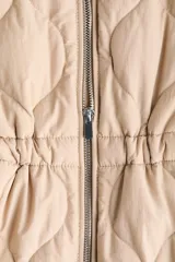 Campera acolchada de nylon beige con diseño guateado, cuello redondo y cierre frontal. Cuenta con hombros caídos, mangas largas, bolsillos laterales y cordón de ajuste en la cintura con tiras colgantes.