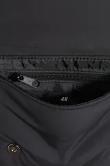 Bandolera negra de tela con correa ajustable con hebilla deslizante y cierre de botones a presión en la solapa.