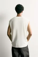 Camiseta tank blanca de corte relajado, con textura en relieve, cuello redondo y sisas amplias. Cuenta con un diseño bordado y estampado en el centro del pecho con las inscripciones "Slow Vibes" y "After Hours" en tonos verde y negro.