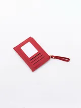 Billetera roja de diseño compacto con cierre superior y bolsillo frontal con botón a presión. Incluye una correa de mano lateral.