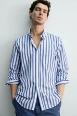 Camisa de corte regular fit confeccionada en tejido de algodón, con diseño de rayas verticales en azul y blanco. Presenta cuello solapa con botones, cierre frontal de botones, manga larga con puños abotonados y un bolsillo en el pecho.