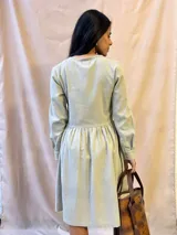 Vestido verde claro de lino, corte a la cintura con falda fruncida, largo a la rodilla, manga larga y abotonado al frente.