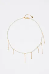 Collar de perlas sintéticas con delicados dijes colgantes de cadenas metálicas doradas. Cuenta con cierre de mosquetón y cadena de alargue con pequeño dije con detalle esmaltado.