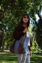 Bolso tipo tote de gran tamaño, confeccionado en una combinación de cuero marrón y gamuza celeste. Presenta un diseño de franjas verticales, con asas resistentes y un bolsillo interior para mayor funcionalidad.