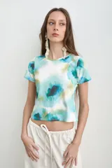 Remera de manga corta con estampado estilo acuarela en tonos de turquesa, verde y blanco, de cuello redondo y corte ajustado.