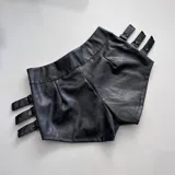 Short negro de cuero sintético con hebillas decorativas en los laterales.