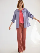 Chaqueta de lino color azul lavanda, de corte holgado, con escote redondo, cierre frontal con botones y mangas ajustables. Presenta un diseño versátil con bordado en la espalda.