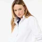Blusa blanca de manga larga con cuello alto con volantes y cierre frontal de botones con ribetes dorados.