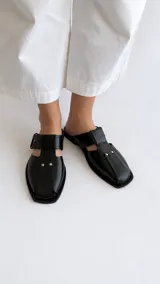 Sandalias de cuero negro estilo fisherman, con punta cuadrada, tiras cruzadas en el empeine, hebilla de ajuste lateral y detalles de tachas plateadas.