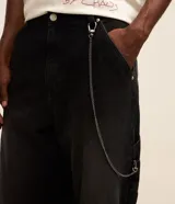 Pantalón de jean corte super baggy con efecto jaspeado o mármol, cintura con trabillas, cierre tradicional y bolsillo cargo lateral con cadena decorativa.