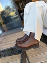 Chaleco tejido de punto en color chocolate, con cuello redondo y diseño sin mangas. Presenta un aplique frontal decorativo compuesto por tres figuras en forma de rombo en tonos tierra, bordeadas con hilo crudo.