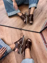 Sandalia de cuero color marrón chocolate, con tira ancha sobre el empeine, hebilla dorada al tobillo y suela track.