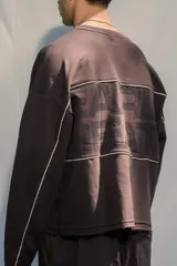 Buzo crewneck color chocolate, de tela rústica liviana, con estampado en el frente y la espalda. Presenta líneas blancas decorativas en el pecho y los brazos, y bordes deshilachados en los puños y el dobladillo.