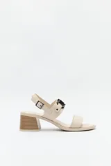 Sandalia color beige con taco medio y tiras anchas cruzadas. Presenta hebilla lateral y herraje metálico en el empeine.