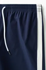 Short de baño azul marino con bandas laterales blancas, cintura elástica con cordón de ajuste blanco y dobladillo curvo.