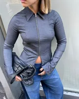 Camisa de manga larga entallada, color gris oscuro, con cuello clásico y cierre frontal de cremallera metálica que permite una apertura inferior.